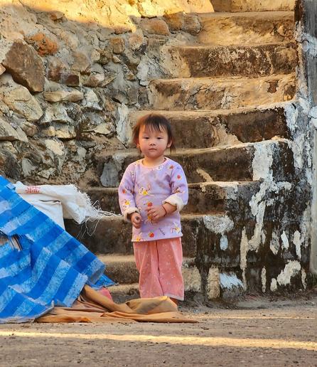 Young Hmong girl wearing colorful pajamas standing at the base of stone stairway.