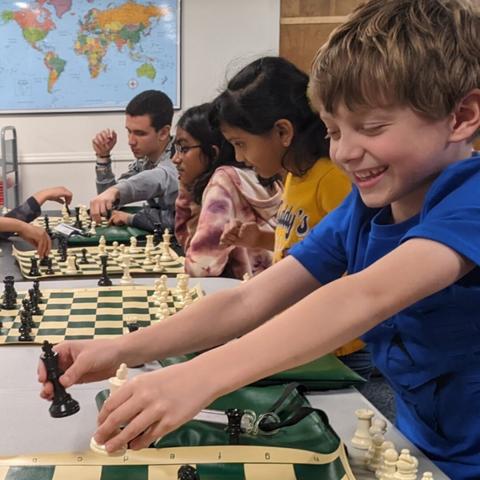 a young boy plays woth chess pieces. he is in the foreground and several other games stretch behind him.