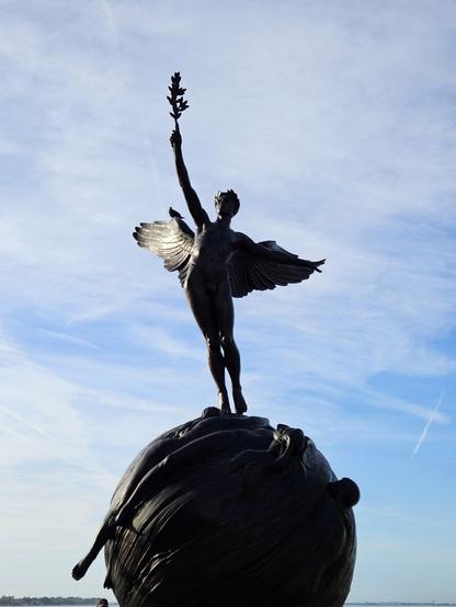 A winged man stands atop a globe while reaching upwards with an olive branch.