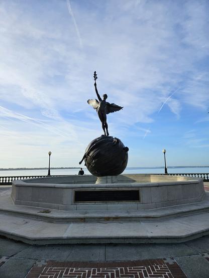 A winged man stands atop a globe while reaching upwards with an olive branch.