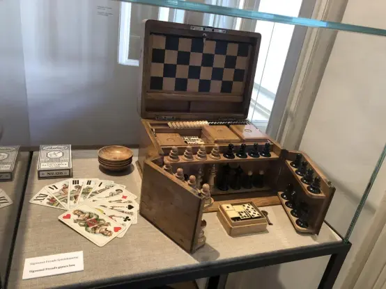 A fold out chess box on display in a museum. The front of the box opens in wings to reveal white and black pieces, and the lid lfts up to reveal a half-board.