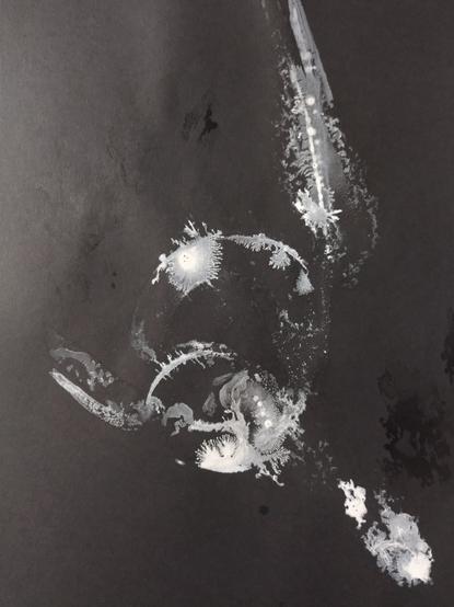 White ink draws several curvy patterns with different shades of white on black paper.