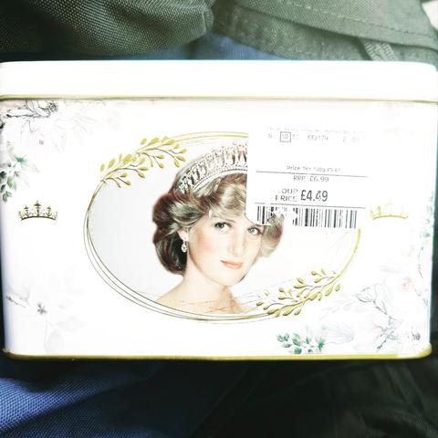A white tin of teabags with pictures of Princess Di on it surrounded by gold filigree