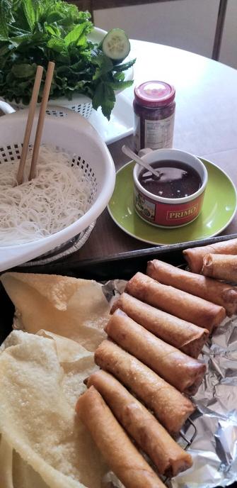 Vietnamese fried Spring rolls, rice vermicelli, nuoc cham sauce & fresh greens & cucumber on kitchen table. Lunch meal.