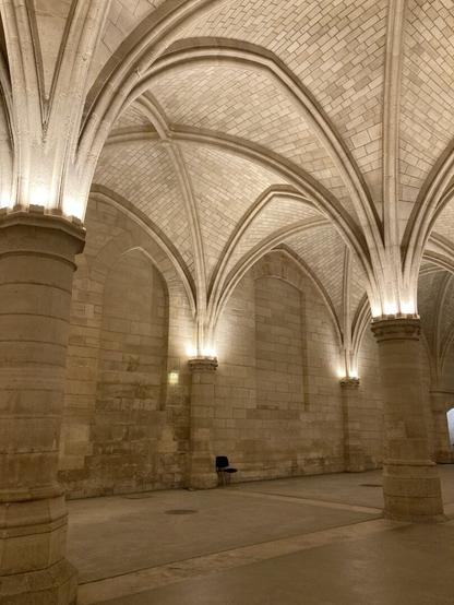 a single, modern black chair sits unattended under lit monochrome vaulted ceilings inside the Palais de Justice in Paris.