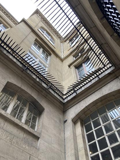 A patch of gray sky peaks between iron spikes discouraging any thought of upward escape along the monochrome, windowed interior walls of the women prisoners courtyard.