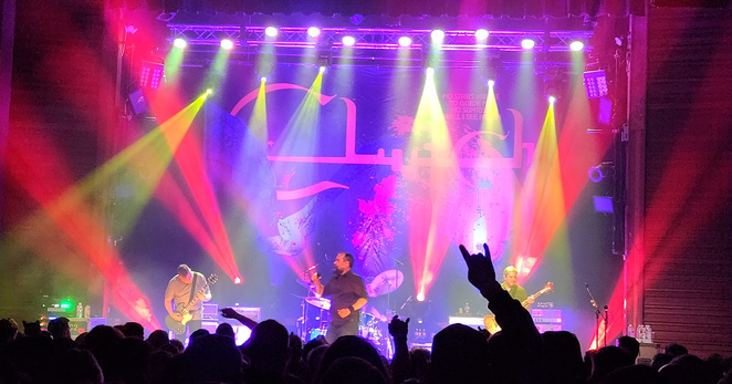 The lead singer for Clutch strutting on stage beneath yellow, red and violet beams of light