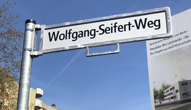Bild zeigt Straßenschild mit dem Namen „Wolfgang-Seifert-Weg“, im Hintergrund sind Hochhäuser zu erahnen und das Baustellenschild des neu gebauten Leonardo-da-Vinci-Gymnasiums.