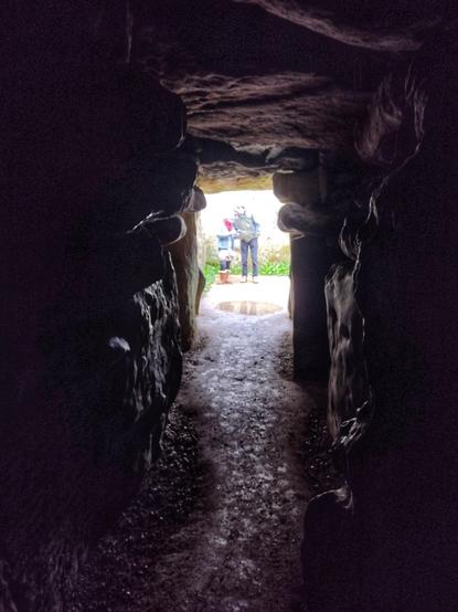 A view from within the dark burial chambers of West Kennet long barrow. A couple can be seen in the entrance way of the chamber.