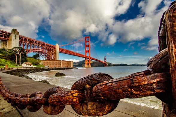 Golden Gate Bridge and Ft Point

This is an image of the Golden Gate Bridge, Ft. point, and the San Francisco Bay. The bottom of the image is of an old, rusty, weather worn, heavy duty chain. 
On the other side of the chain is a waved splashed walkway leading out to Fort Point. To the right of the walkway is the water of San Francisco Bay.
Ft. Point is itself framed from above by the Golden Gate Bridge. The bridge stretches across the image diminishing off into the distance right/center of the image with the Marin Headlands in the background.
The sky is partially cloudy adding a little bit of a dramatic effect to the sky.