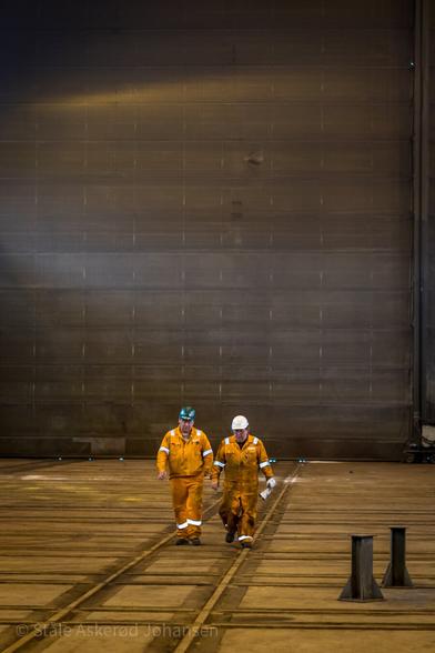 Two men walking on a floor in an industrial building.