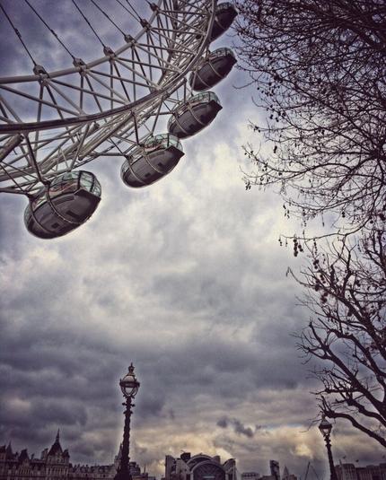 The London Eye ferris wheel in London, GB, with a dramatic sky and parts of the city‘s skyline in the background.