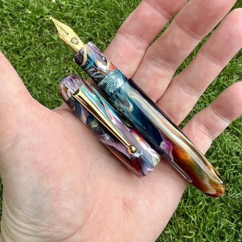 Colorful Zephyr pen model, uncapped, in maker’s hand, against a green grass background.