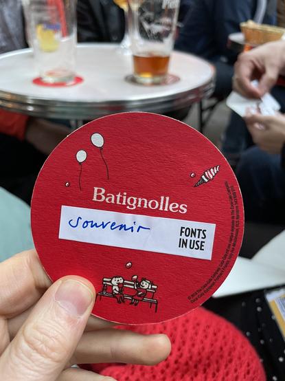 Photo of a beer coaster with the Batignolles logo and a paper label beneath it with a Fonts In Use logo and handwritten “Souvenir”.
