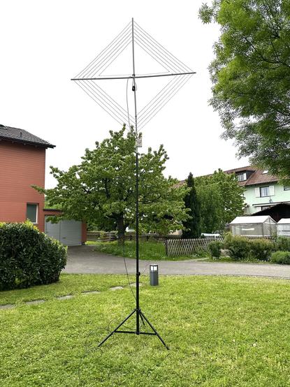 Photo of a 80m frame antenna (mag loop) on a tripod standing on a patch of grass in the backyard.