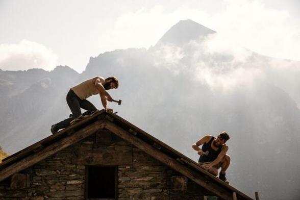 Two men working on building the roof of a cabin in the mountains in The Eight Mountains