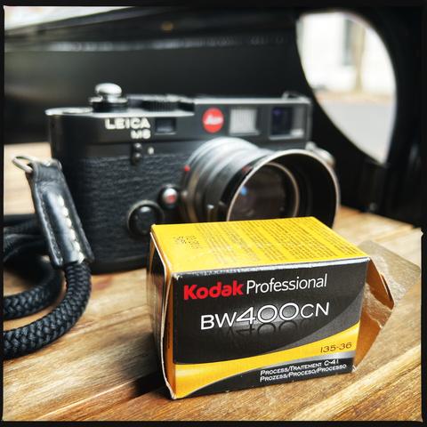 A black film rangefinder camera in the background, on a cafe table. In front, a film box saying “Kodak Professional BW400CN”.