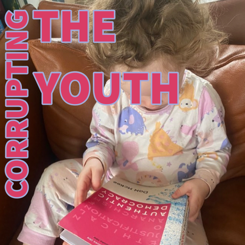 The words “corrupting the youth” are placed over an image of a young toddler reading DaN McKee’s book, Authentic Democracy: An Ethical Justification of Anarchism