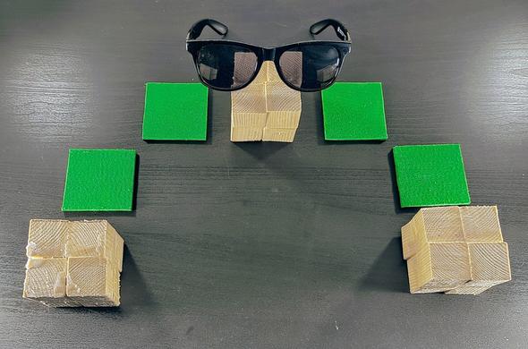 Eurovision 2023 Käärijä costume made out of neon green felt patches, wooden cubes and sunglasses on top of a black table.