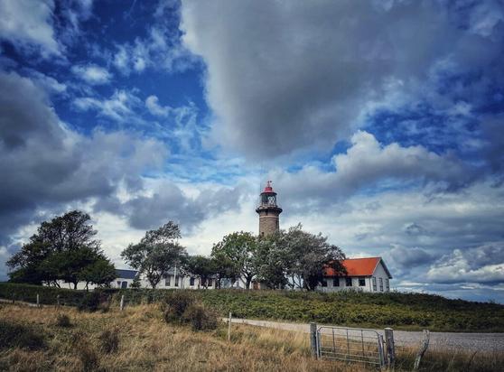 Photo of Fornæs Fyr (near Grenaa, Denmark), a lighthouse made of brown bricks, with a bright blue sky and some large white clouds in the background.