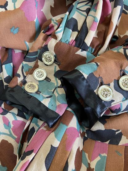 Close up of the cuffs of a dress in patterned turqoise, pink, brown, black and cream fabric. The cuffs are repaired with black satin ribbon.
