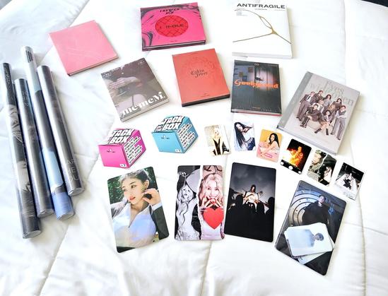 A collection of k-pop albums, posters, and photos spread out on a white bed spread.