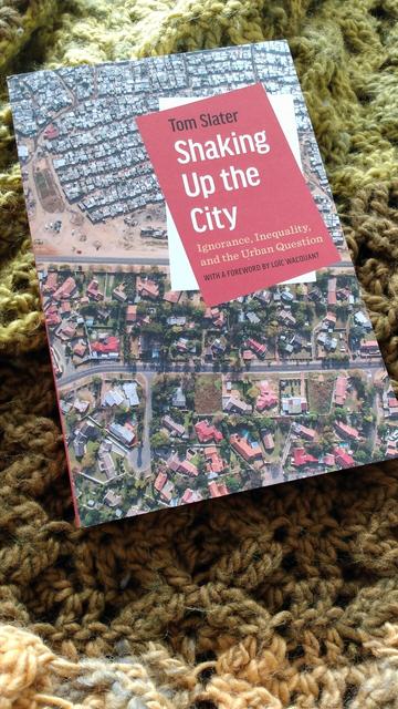 Book cover for Shaking up the city: ignorance, inequality, and the urban question by Tom Slater. Cover image shows an aerial shot of urban development divided by a road. On one side are densely packed informal housing. On the other are large suburban homes with green yards and pools.