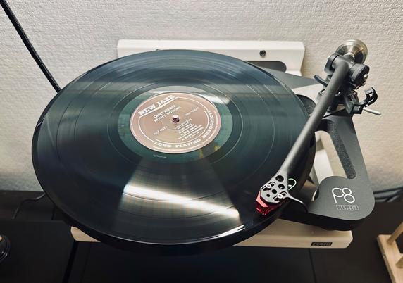 Photo of a record spinning on the skeletal plinth of a Rega P8 turntable. 

The tonearm is extended and tracing the opening track.