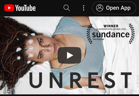 Screenshot of the cover image of the documentary film Unrest on YouTube. The image is of a woman laying in a bed looking up at a camera with electrodes on her head. In the upper right corner is a logo noting the film as a winner at the Sundance Film Festival