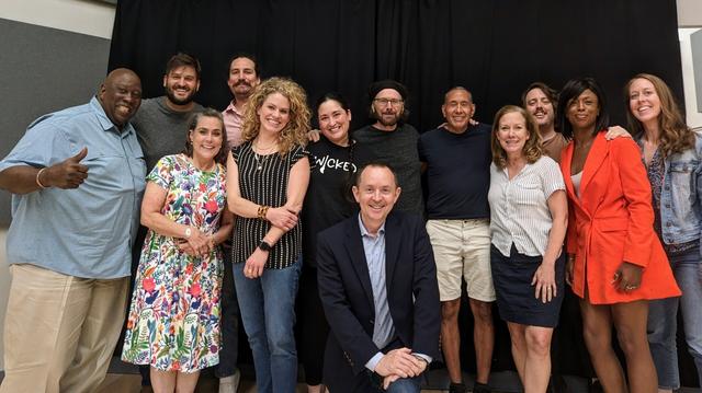 Photo of about a dozen people, all smiling and posing in front of a black curtain.