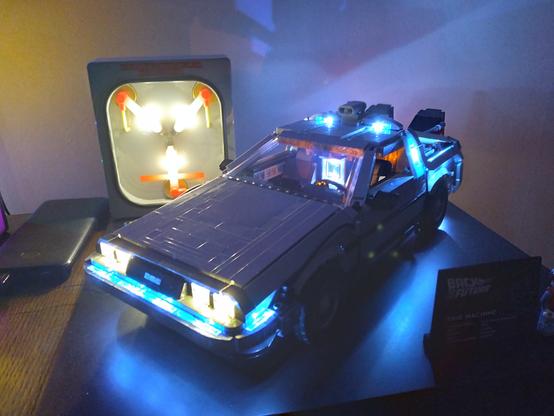 This Lego Back to the Future DeLorean time machine has LED lit headlights and Flux bands - a Y-shaped LED flux capacitor is lit behind it, offset to the left.