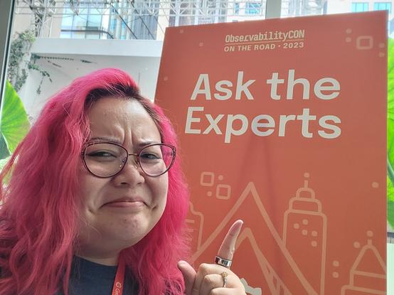 Nicole making a dubious face and pointing at the Ask the Experts sign.