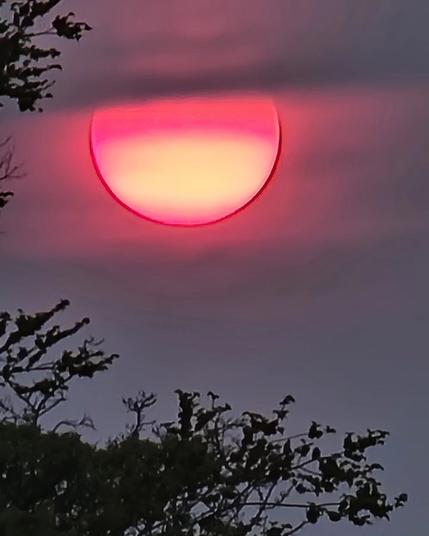 The top of the sun is covered in grey smoke. The bottom is yellow lined with red with a hot pink glow around it.