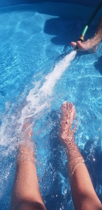 My feet in blue plastic kiddie pool with a friend running hose on full spray.