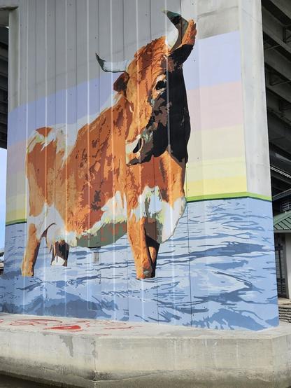 Painted on the vertical support piles of a large bridge, cattle wade in shallow water.