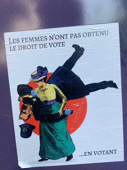 Sticker on a wall of a victorian comic of a woman throwing a cop and the words “Women didn’t get the right to vote by voting.” in French