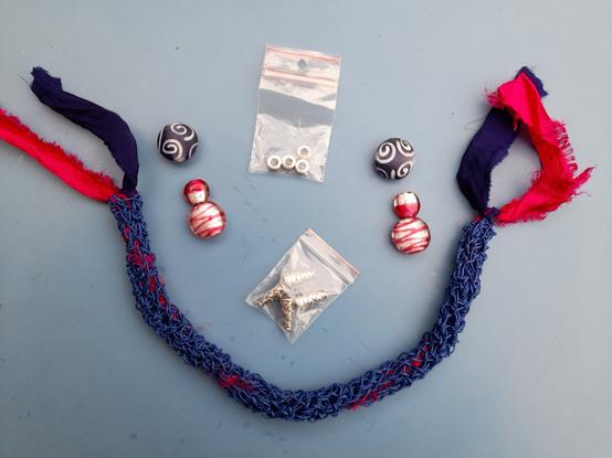 A crocheted blue paper yarn torque looks like a Byzantine wave chain. It's filled with blue and pink saree silk. There are hand-painted glass beads, dark blue with white spirals and glass beads with pink paint and silver inlays. Also, some silver elements to choose from.