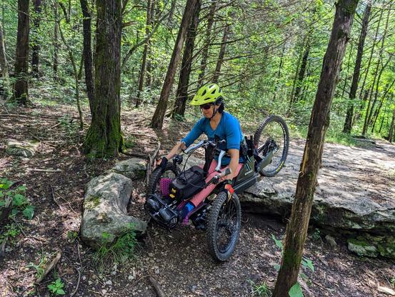 Female writing and adaptive mountain bike over a large rock.
