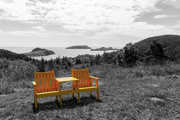 A pair of yellow chairs rests beside a highway lookout over the small town of Tors Cove, Newfoundland. Done in selective colour.