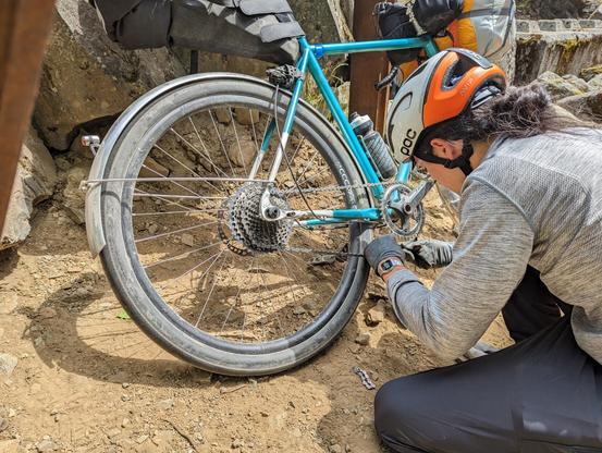 a blue gravel bike with 1x11 Sram Apex 1 drivetrain; the derailleur is strapped to a seat stay; a person is working on making the chain shorter so it goes directly from the chainring to one of the large cogs and back
