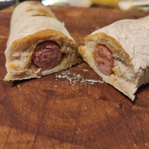 A hot dog, rolled in pizza dough and cooked, cut in half.