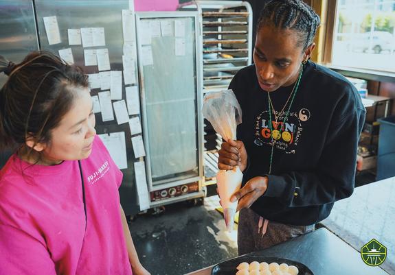 Yvonne Turner (right) holding a piping bag and looking toward owner of Fuji Bakery (left)
