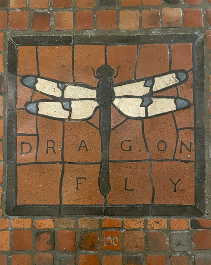 Moravian tile floor mosaic by Henry Chapman Mercer, dragonfly with black body and white wings with blue spots on red tile floor of PA Capitol building, labeled “DRAGONFLY” and numbered “100”