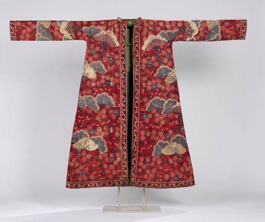A robe of red ground cotton with floral embellishments. Tree fronds in dark blue punctuate the design down the front and sleeves. It is trimmed in a smaller, busier floral print, and lined in green silk.