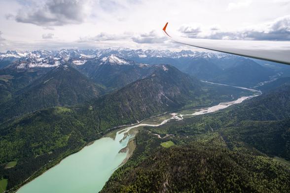This picture shows a river leading into a milky lake with a snow capped mountain range in the background. It was photographed from a glider plane so the wing is visible on the right side of the frame.