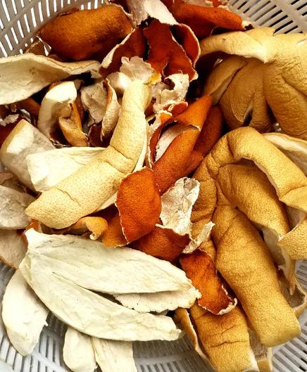 A big plastic collander bowl, filled with assorted dried citrus fruit peels