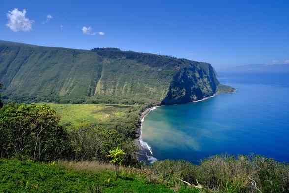 Looking over a large green flat surrounded by steep mountains. The ocean borders the valley and mountains.