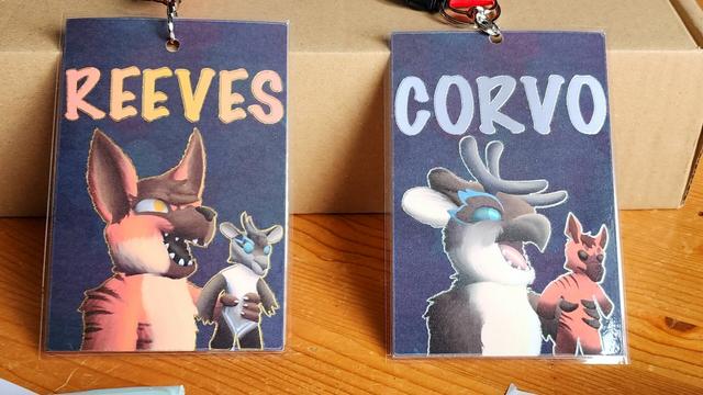 A photo of two convention badges - one of Reeves, an aardwolf, and Corvo, an owldeer.