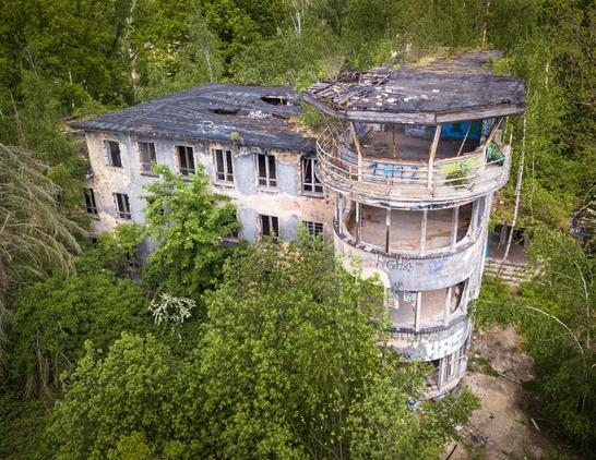 Drohnenfoto einen Lostplaces: Tower eines ehemaligen Militärflughafens. Alle Fenster sind rausgeschlagen, das Dach ist noch halbwegs intakt.