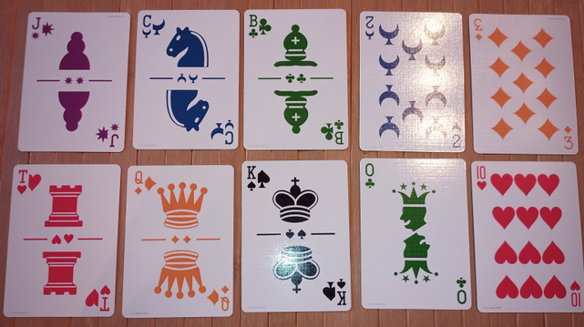 Ten cards from the K6T card deck. Shown are six court cards: the Jack of Stars (in purple), the Cavalier of Moons (blue), the Bishop of Clubs (green), the Tower of Hearts, the Queen of Diamonds (orange), and the King of Spades (black). Also shown is a Joker (zero) of Clubs, and three cards from the dozenal expansion pack: the dek of moons (the numeral is a turned two), the el of diamonds (turned three), and do of hearts (10; rhymes with 'no'.)